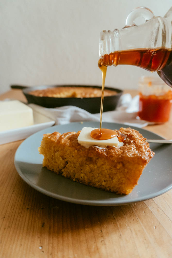 a slice of cornbread on a plate with syrup being drizzled on top